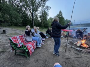 Ognisko na plazy. Dookoła siedzą uczniowie i nauczyciele. 