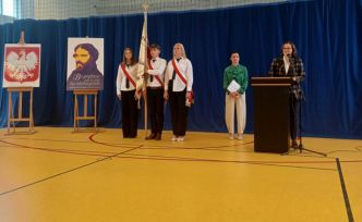 Na hali gi,nastycznej uczniowie w poczcie sztandarowym , Dyrektor i Wicedyrektor. Z lewej strony godło Polski i portret Norwida.