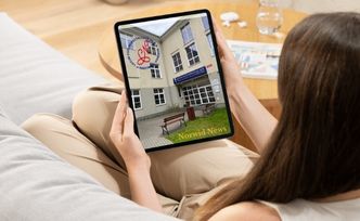 Dziewczyna siedzi na kanapie, trzyma w rękach tablet z okładką szkolnej gazetki.