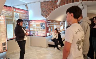 Sala z sufitem w kształcie łuków zaadoptowana na galerię sztuki. Uczniowie słuchają wykładu.