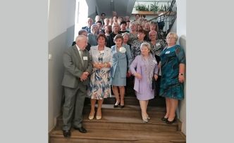 Grupa kilkudziesięciu osób stoi na drewnianych schodach.
