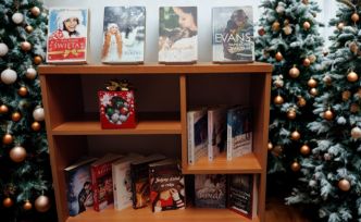 Regal z książkami i pudełkiem z czekoladowymi kulkami. Dookoła choinki świąteczne.