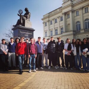 Grupa młodzieży pozuje do zdjęcia przed Pomnikiem Kopernika w Warszawie.