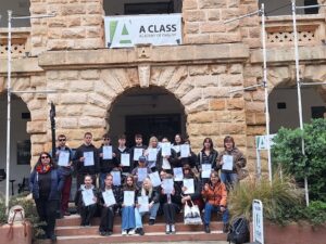 Grupa uczniów pozuje do zdjęcia na tle budynku, w rękach mają dyplomy.