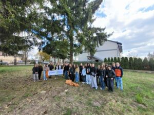 Duża grupa uczniów na trawniku pod drzewem.