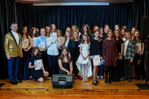 Duża grupa młodych osób prezentująca dyplomy podczas zdjęcia grupowego.