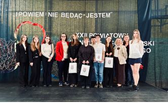 Uczestnicy i opiekunowie konkursu stoją w jednym rzędzie na tle dekoracji scenicznej, patrząc w stronę aparatu.