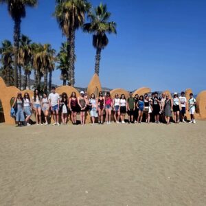 Zdjęcie grupowe na plaży, w tle niebieskie niebo i palmy oraz napis.